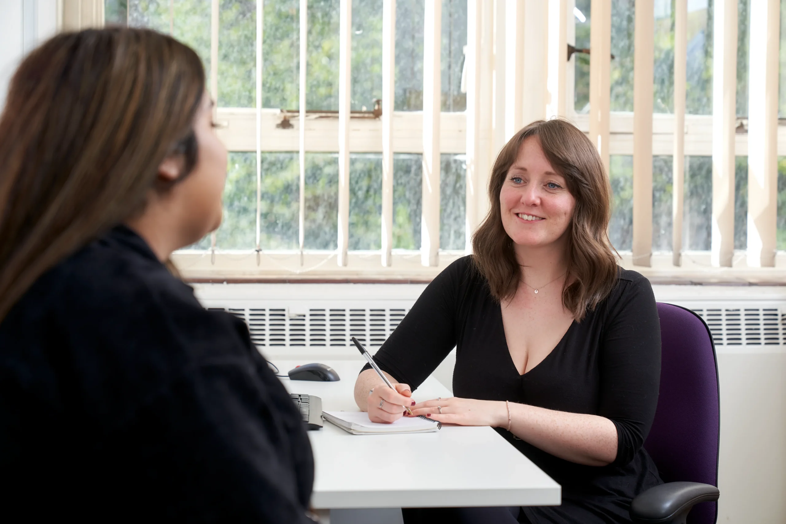 The 101 guide to becoming a psychologist - two women in black talking at a desk with a notepad