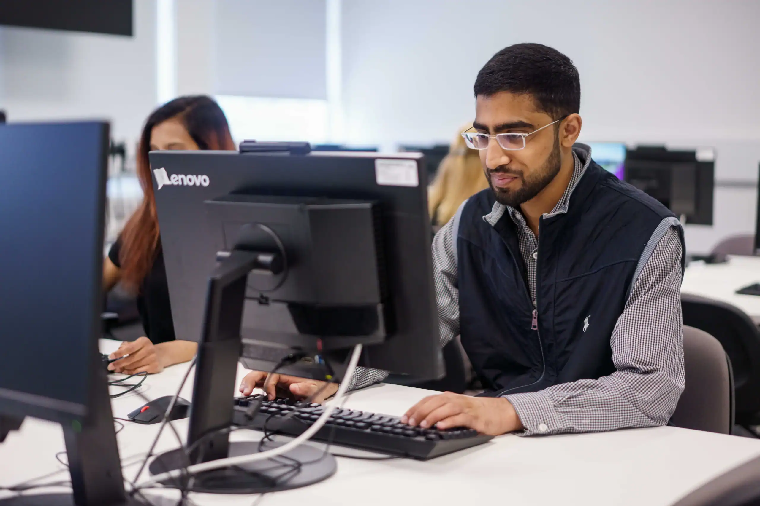 Cybersecurity in the age of AI – threats and solutions - man wearing glasses facing a computer in a computer lab