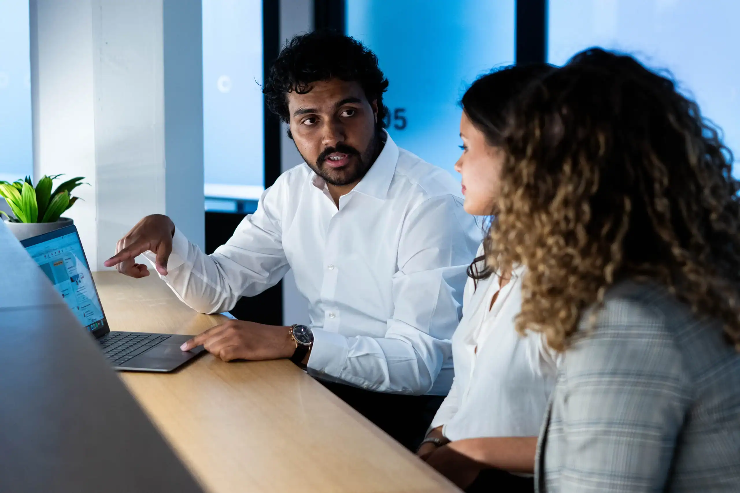 Doctor of Business Administration: The benefits of professional doctoral study -man in white shirt facing two women mid-conversation in front of a laptop and a screen