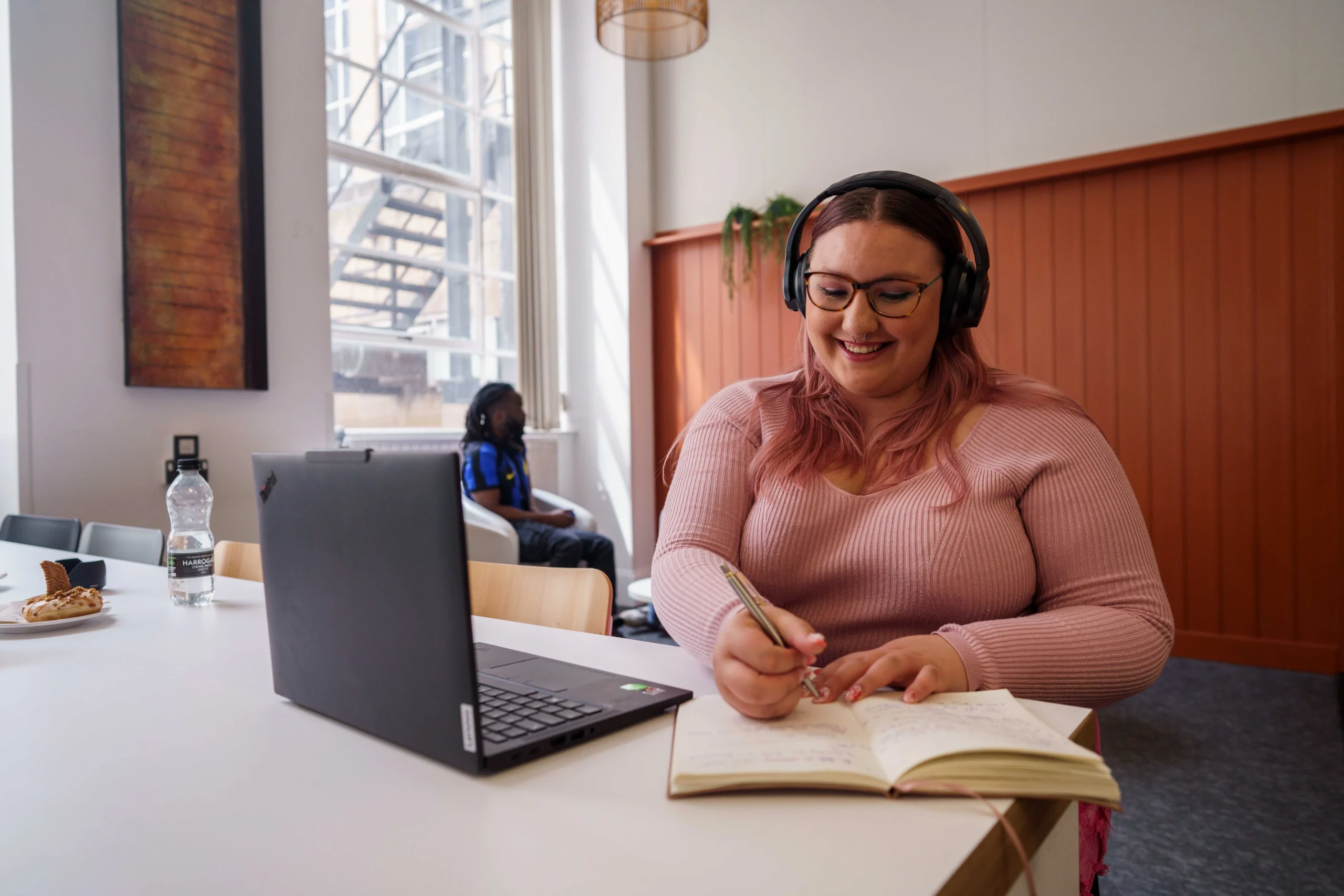 Shape public health systems with an online Master of Public Health - smiling woman with headphones writes in notebook in front of laptop