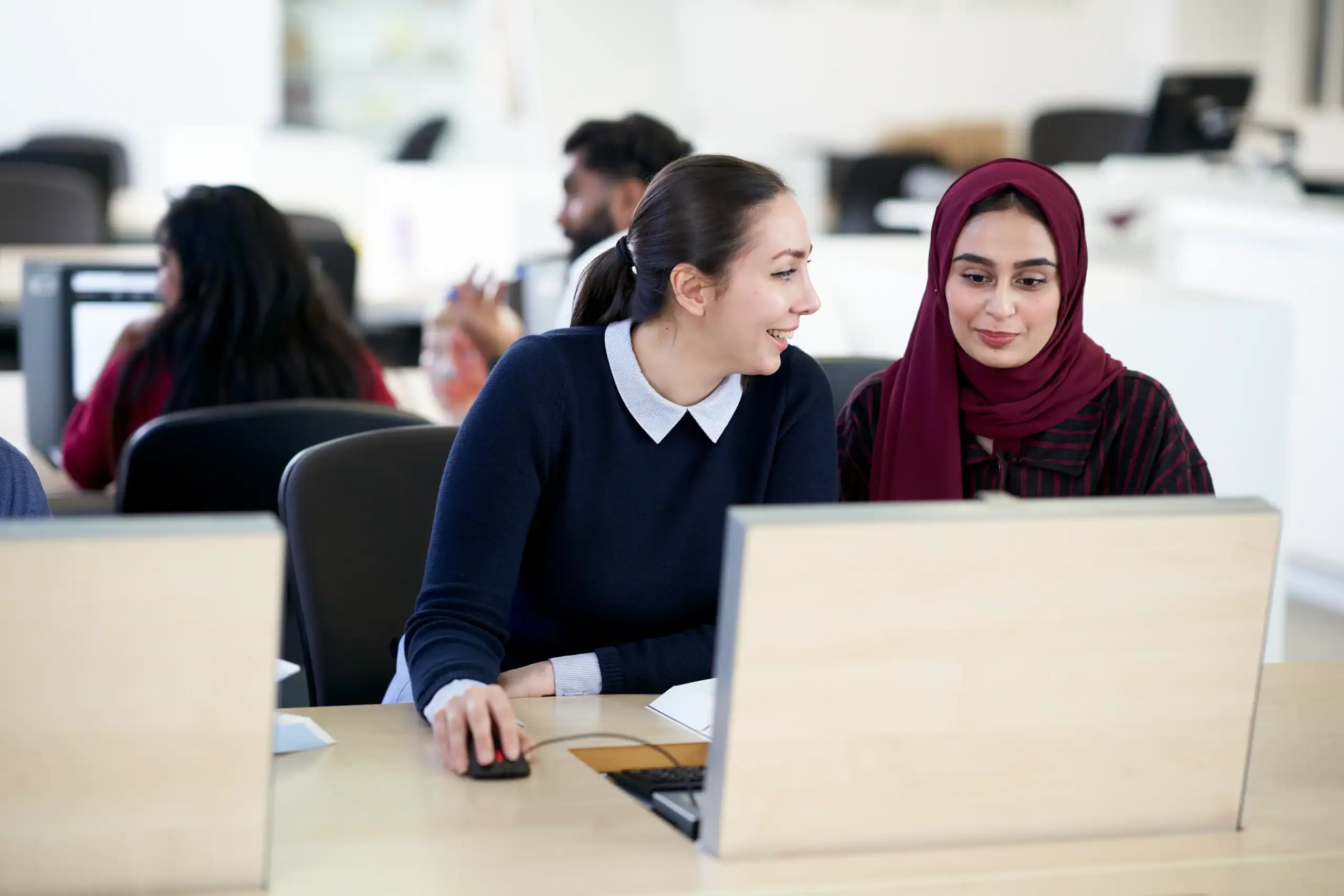 two woman working together mid-discussion over one laptop