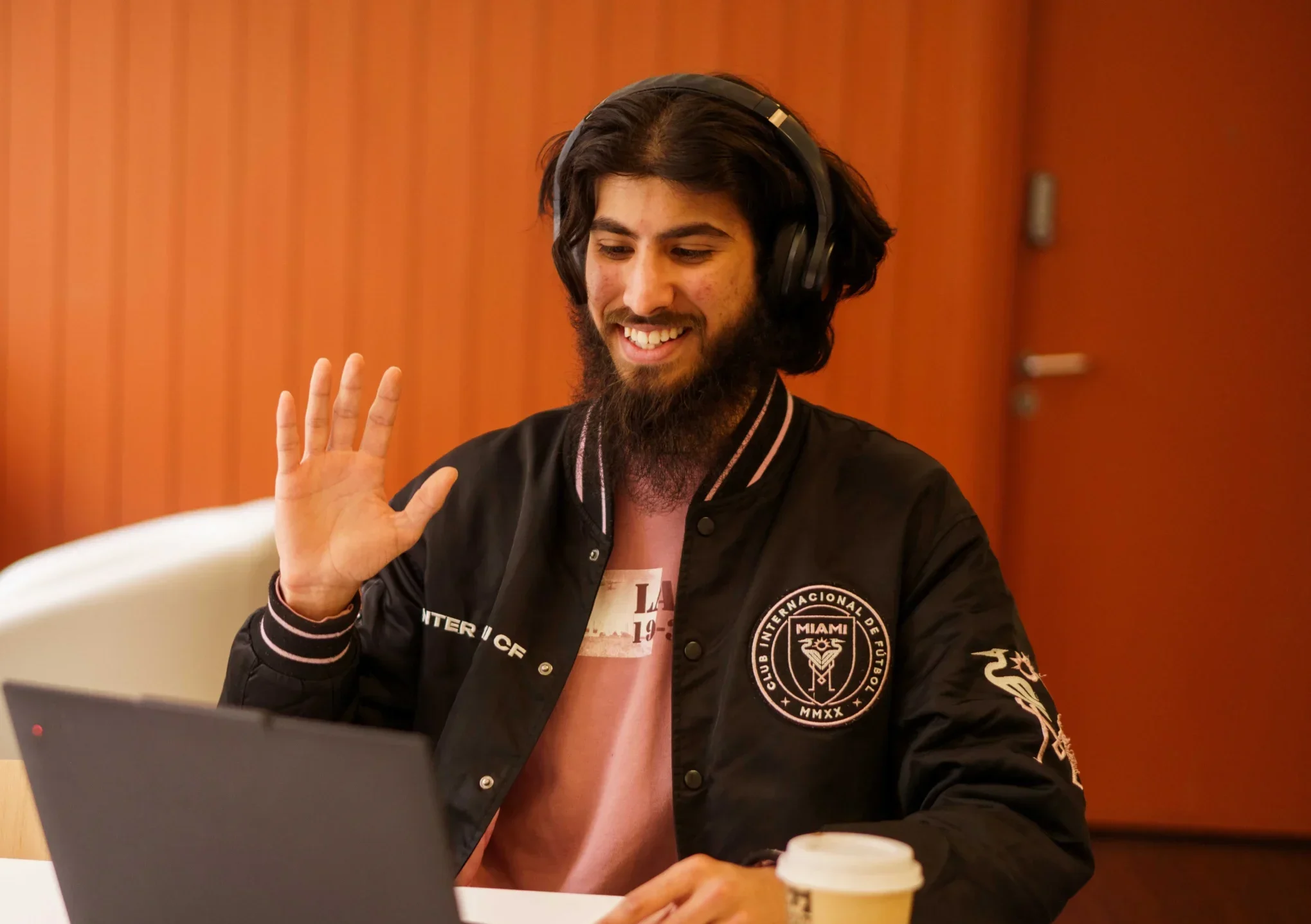 Your online tutor - man wearing headphones waves at laptop while meeting with online tutor